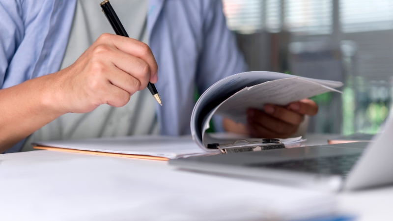 Osoba pregleda dokumenta i beleži podatke uz laptop, što prikazuje rizik grešaka kod samostalnog vođenja knjiga